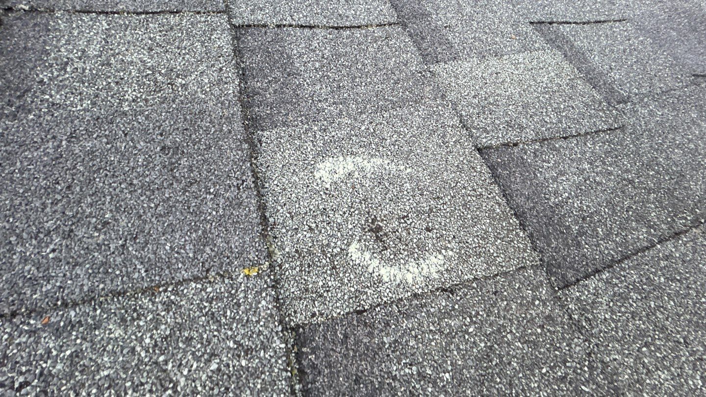 Close-up of a hail impact mark on an asphalt shingle showing granule loss, found during a KO Roofing storm damage inspection in Plattsmouth, NE